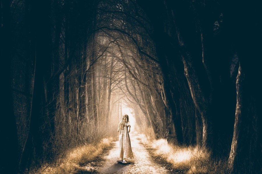 Μια γυναίκα με λευκό φόρεμα σε ένα μονοπάτι ενός σκοτεινού δάσους